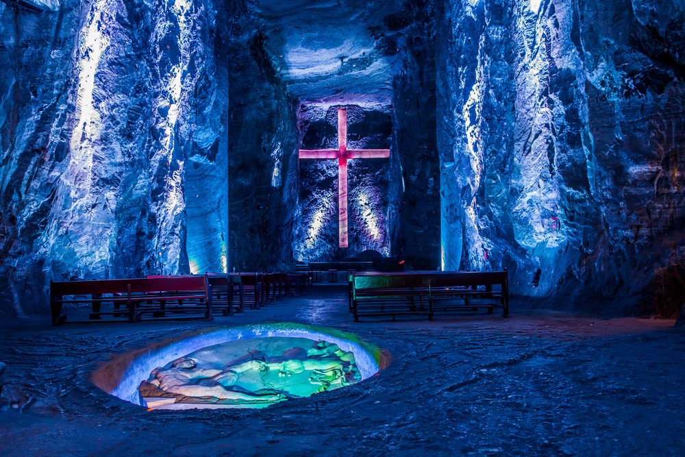 An underground chapel showing a large glowing cross and pews.