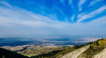 View from the peak of a mountain in the Sierra Nevada, overlooking a mountainous range and with blue skies above.