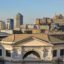 Rooftop view of Genoa Train Station with tall buildings behind and blue skies above.