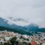 Colorful buildings scattered at the bottom of large mountains with clouds surrounding the peaks in Quito, Ecuador