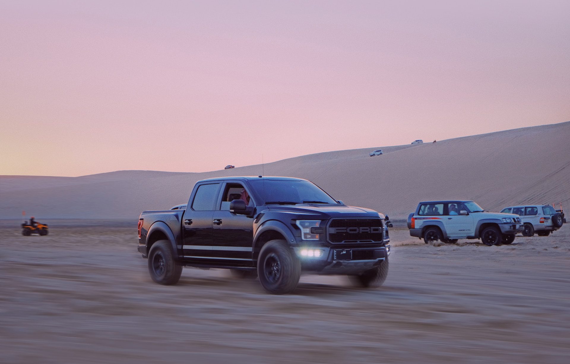 4x4s driving fast across the desert at sunset.