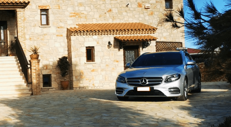 Zakynthos Airport Taxi (Sedan) Welcome pickups A silver Mercedes Zakynthos Taxi parked outside of a stone-walled villa.