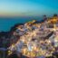View from Oia, with buildings on the cliff edge looking out towards a blue sea at sunset.
