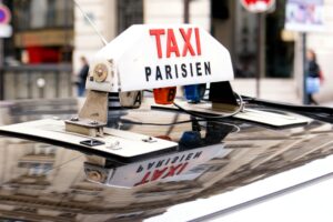 A white Paris Taxi sign with red lettering on the roof of a taxi.
