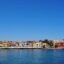 View of Chania from the water, with colourful houses lining the waterfront and blue skies above.
