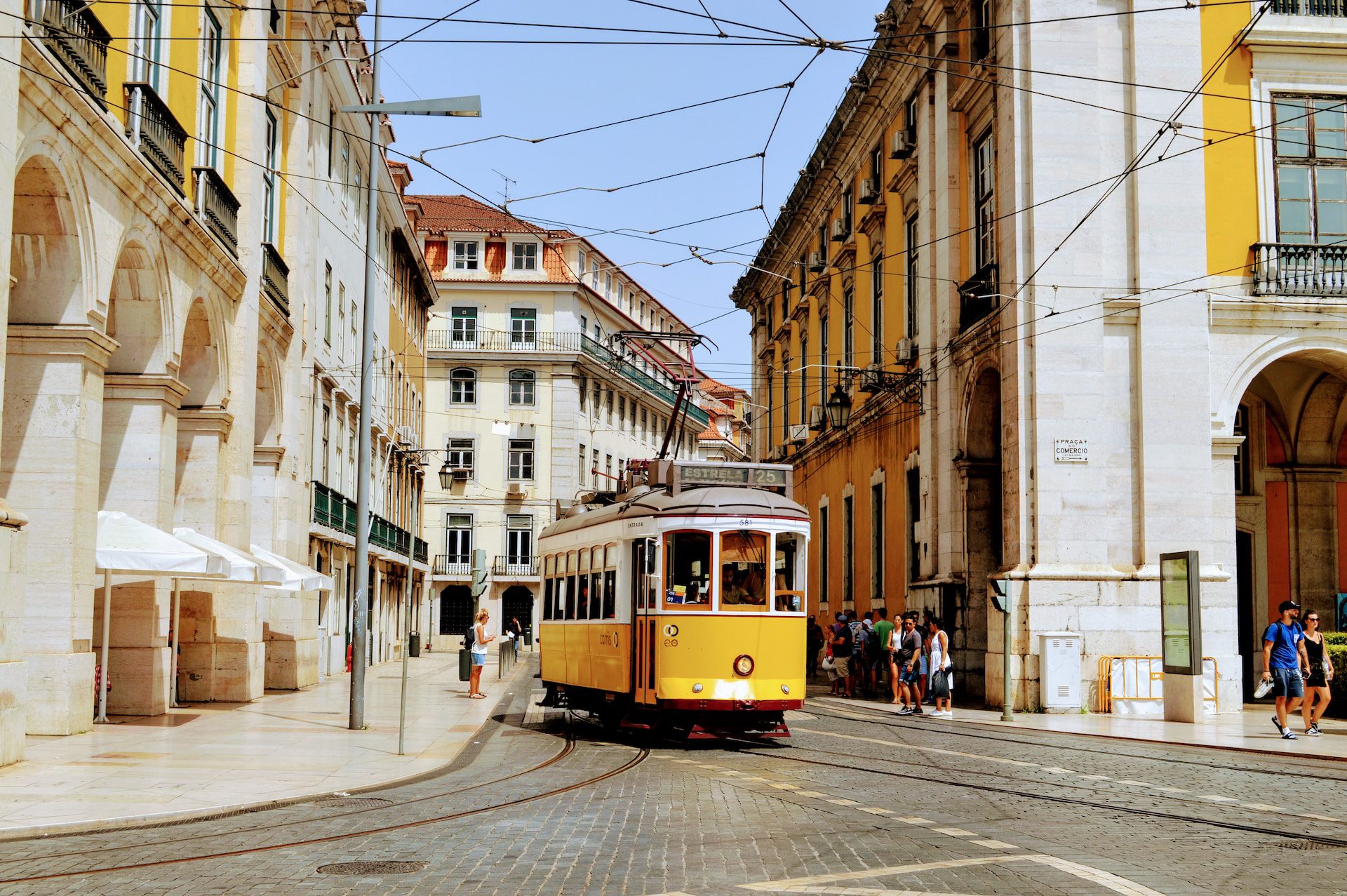 A yellow tram in Lisbon city centre, with houses on both sides and blue skies above.