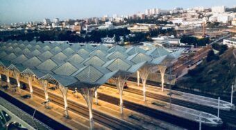View of a roof canopy above Oriente Train Station, with blue skies above and houses in the distance.