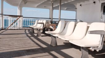 A ferry deck with plastic white chairs in a line and blue sea and skies in the background.