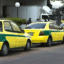 Yellow taxis with a green stripe lined up outside of a building.