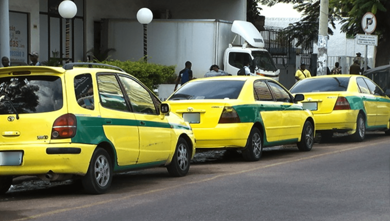 Taxi Maputo Yellow taxis with a green stripe lined up outside of a building.