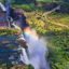 Aerial view of Victoria Falls, with water cascading into a canyon on the left, a rainbow in the centre, and green landscape on the right.