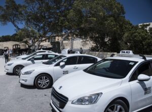 Taxis in Malta - Welcome Pickups A line of white Malta taxis parked under the shade of a tree.