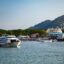 View of Rassada Pier, with a small ferry sailing past, with boats docked behind and mountains in the distance.