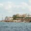 Scenic daytime view of the rocky coastline and waterfront near St Julian's, Malta, with the sea in the foreground and buildings along the shore, capturing the coastal atmosphere travelers enjoy when heading to St Julian's from Malta Airport.