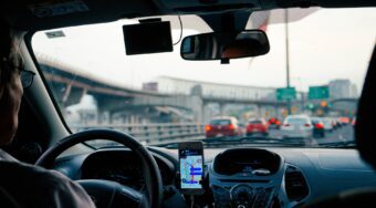 A person driving in their car, with a phone with GPS next to the steering wheel and traffic up ahead.