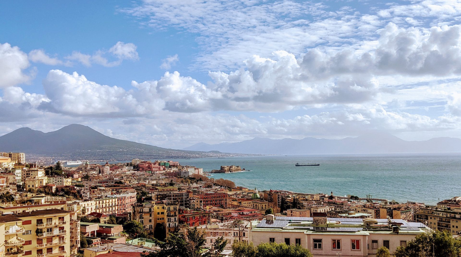 View of the city of Naples, with mountains in the background and the sea up ahead.