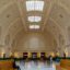 The interior of a wide white-domed building with large wooden benches.