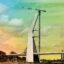 A long bridge with a hundred meter tall construction in the centre supported with cables against a rainbow coloured sky.