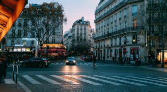 A street in Paris city centre, showing buildings either side, a zebra crossing, and black cars on the road.