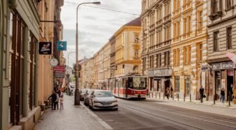 View of a street in Prague, with a tram on the right side of the road and cars and taxis on the left.
