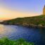 Greenery and blue waters in the forefront of a hillside ocean view with a monument atop the high point.