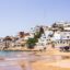 View of the Taghazout coastline with a golden sandy beach and houses going up the hill to the right.