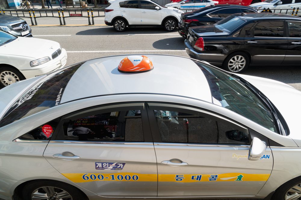 Busan taxi A white Busan taxi with an orange taxi light on the roof and a yellow strip across the doors with the company details displayed on it.