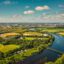 Aerial view of fields, trees, and a river under a blue cloudy sky.