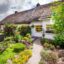 Two white homes in Adare, Ireland are adorned with yellow framed windows and vibrant gardens lined with a walkway.