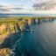 The stunning cliffs of Moher stretch under a cloudy daylit sky alongside calm waters.