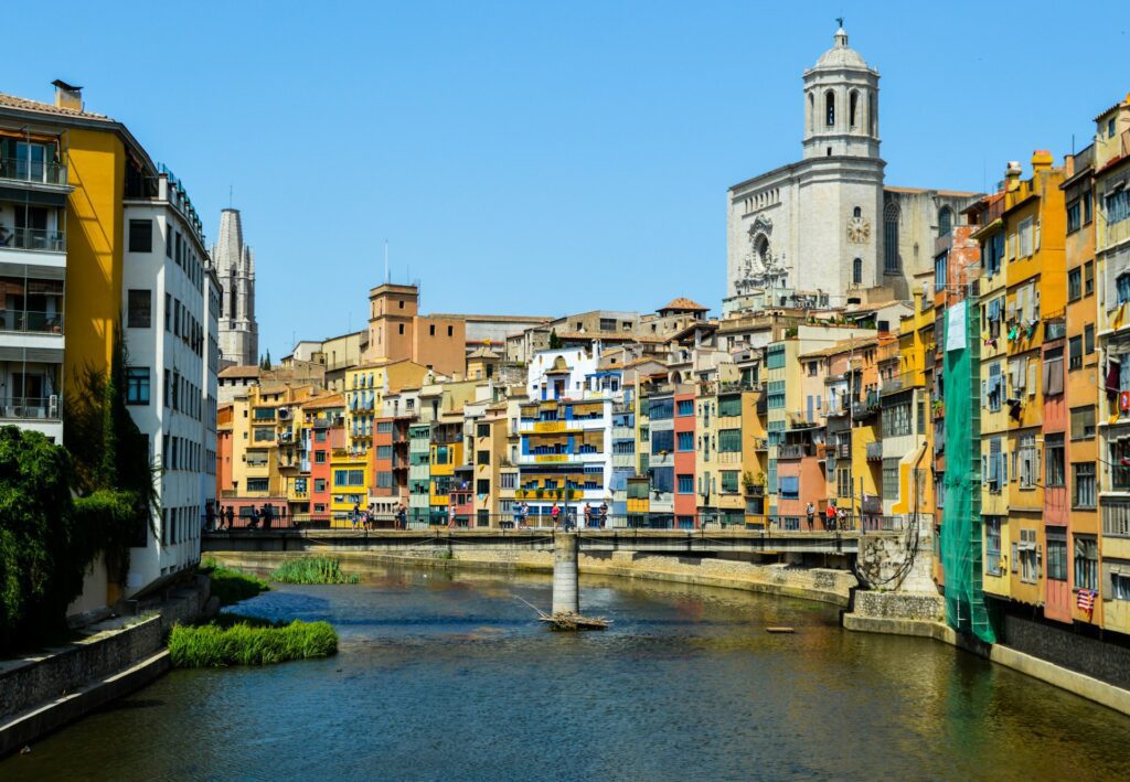 Colorful buildings closely line both sides of a waterway in Girona, Spain.