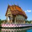 Small ornate temple structure on the corner of a walkway along water above a colourful wall.