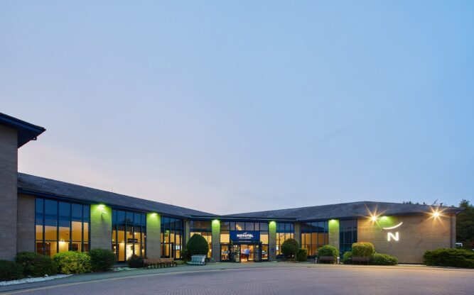 Exterior of Novotel at dusk, with lights on the front of the building.