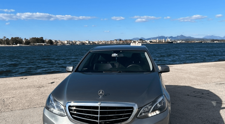Aktion Taxi - Preveza Taxi Silver Mercedes parked in front of a waterway.
