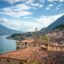 Limone Sul Garda under a sun lit sky displaying the mountains and red roofed homes next to the water.