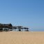 A large beach with a wooden beach hut on flat sandy ground with a bright blue clear sky.