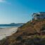 A beach house positioned on a coastal hill to the right, sloping down to a beach on the left.