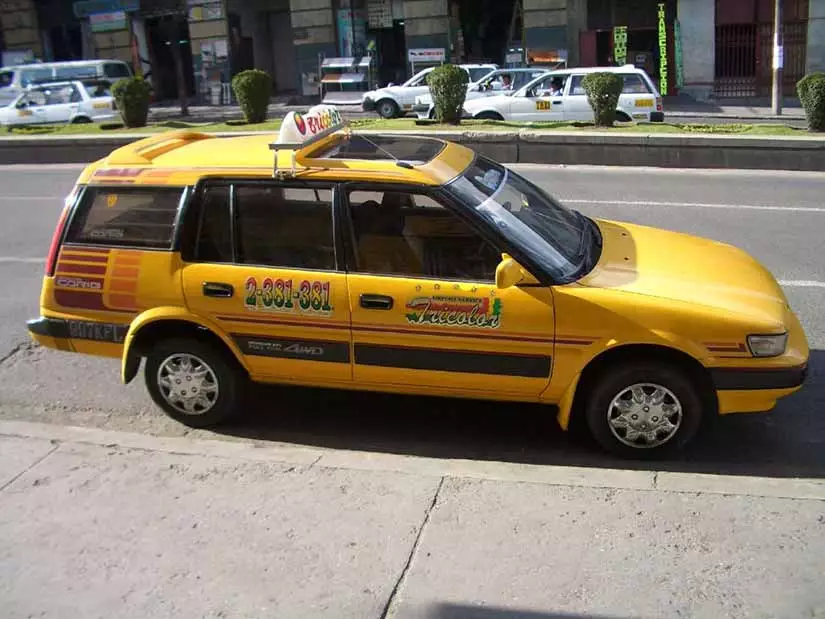 Santa Cruz de la Sierra A yellow station-wagon taxi, with green and red signage displayed along the sides of the vehicle, parked on the street