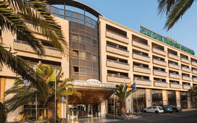 Exterior of Elba Vecindario Aeropuerto Business & Convention Hotel, showing a large sandy-coloured building with blue skies above.