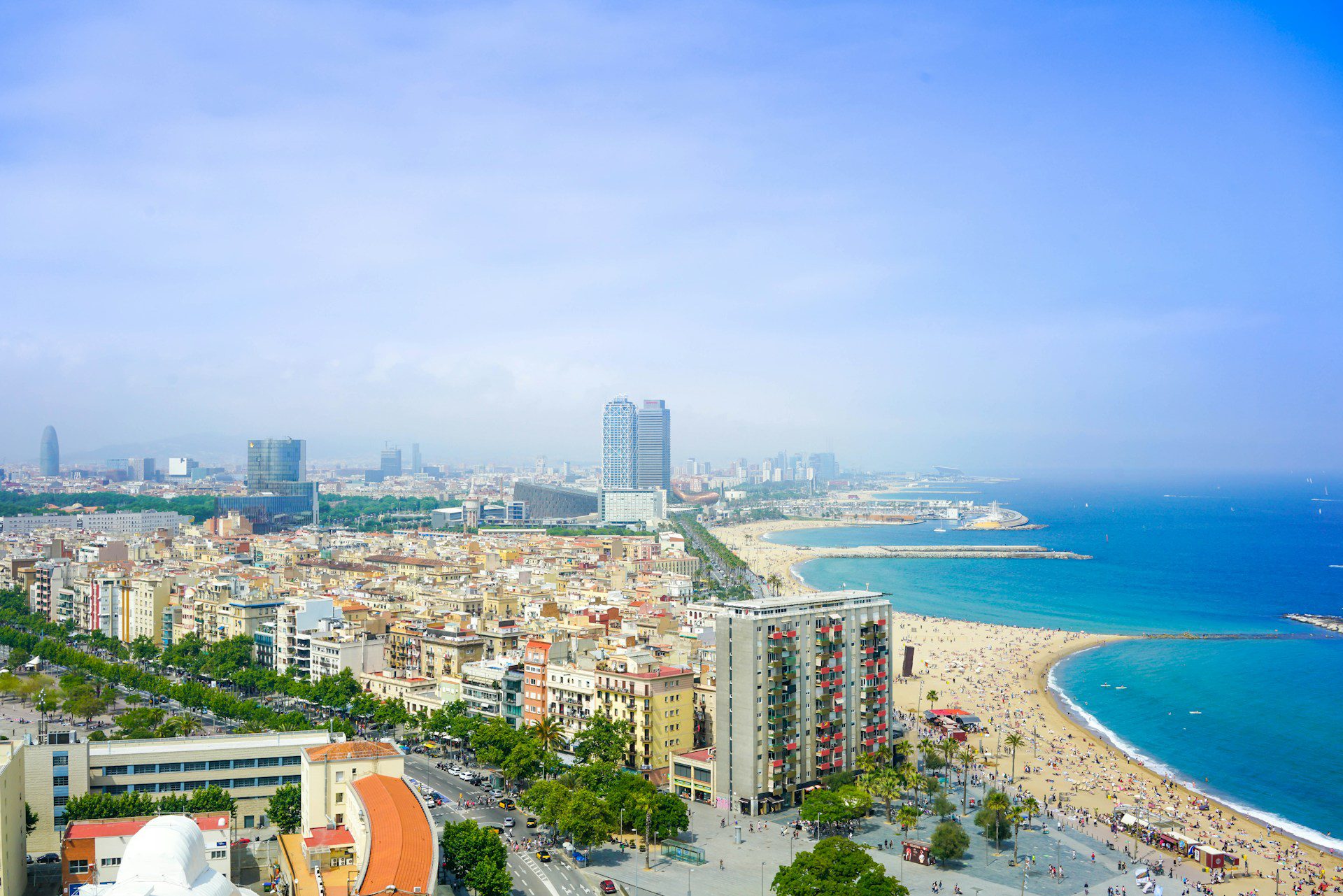 View of Barcelona City Beach, with skyscrapers on the left and a long stretch of sand meeting a blue sea on the right.