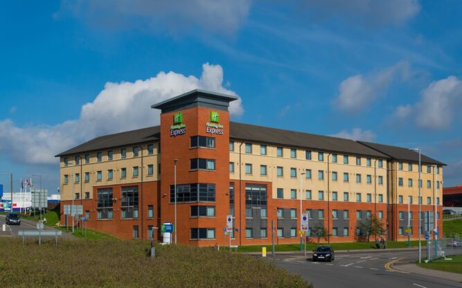Exterior of the Holiday Inn Express at Luton Airport, with blue skies above and green grass surrounding the hotel.