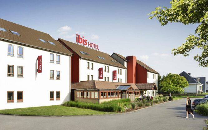 A side view of the ibis Charleroi Airport Hotel painted white with a brown roof and red signage