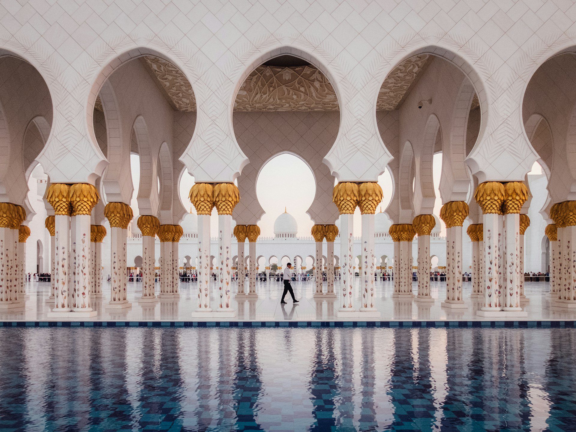 Close up of the Grand Mosque, showing beautiful white and gold columns, with a large body of water in front.