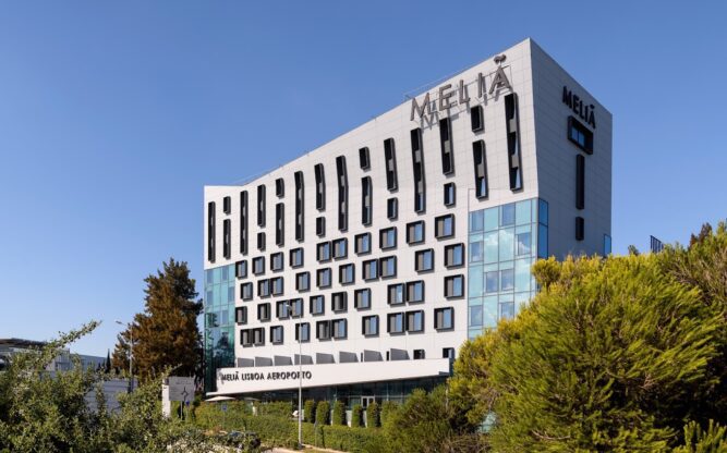Exterior of Hotel Melia at Lisbon Airport, with blue skies above and trees surrounding the building.