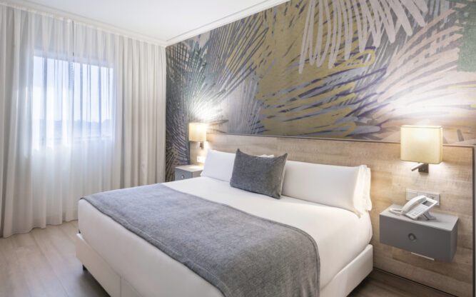 A beige and grey coloured room with a statement wall behind and a double bed in the centre.