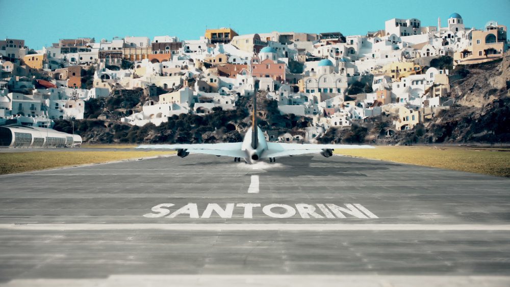 A plane taxis the runway at Santorini Airport with colourful homes in the background.