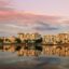 The mirror image of a metropolitan city reflected on the edge of a lake.