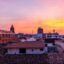 The sun setting in a pink, orange and purple sky over a town with with brown-tiled roofs.