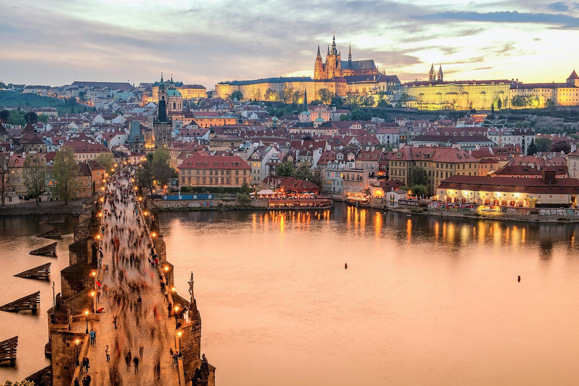 View of Charles Bridge in Prague city centre in the evening, with a body of water on the right and the city up ahead.