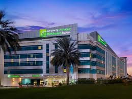 Exterior view of the Holiday Inn Express Dubai Airport hotel at dusk, located near Dubai International Airport, with palm trees and illuminated signage under a twilight sky.